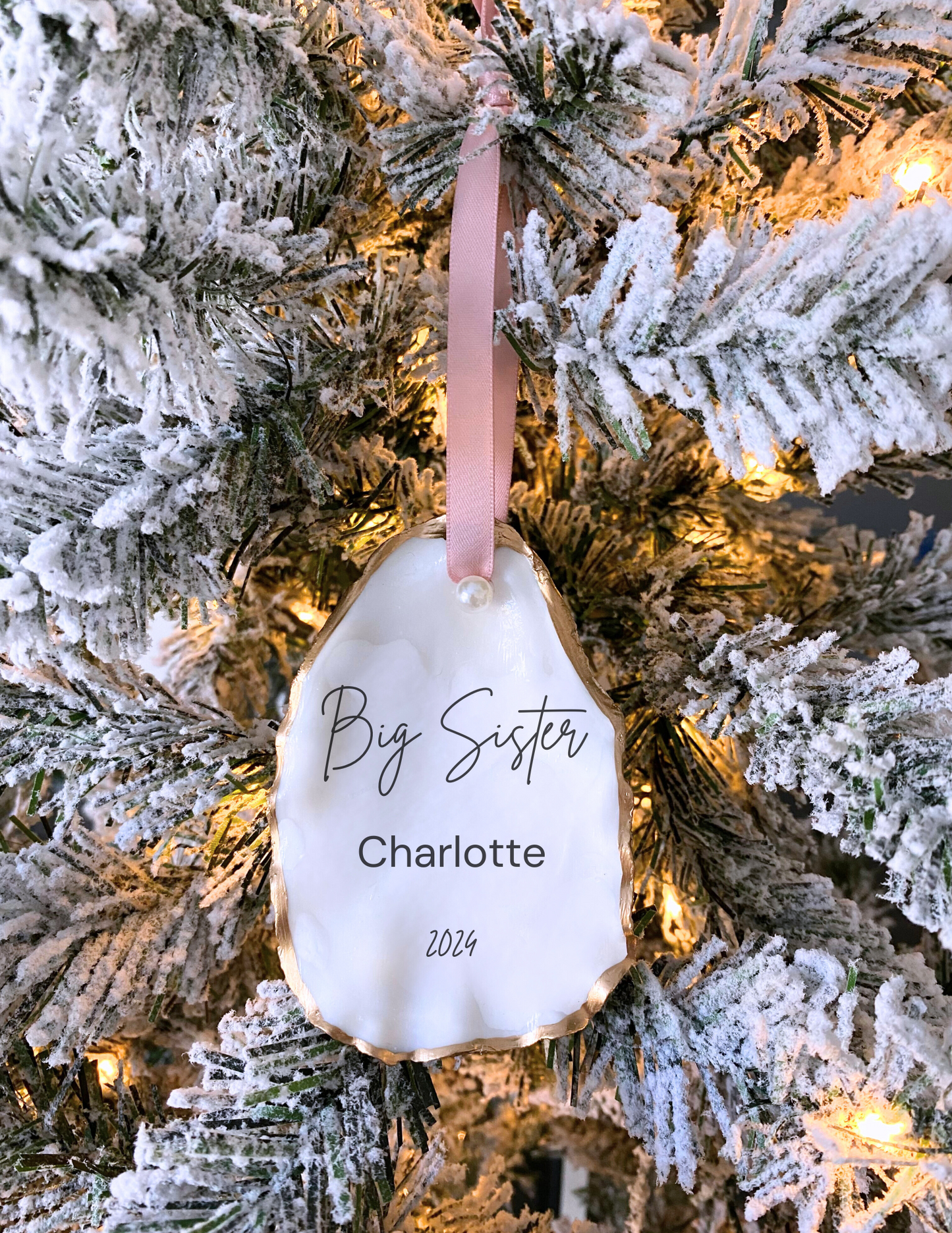 Personalized big sister oyster shell ornament with Sophia in script, pearl finish, gold trim, and pink ribbon hanging on Christmas Tree