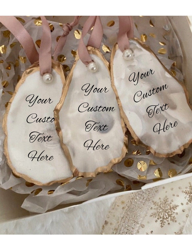 Sets of all natural handmade personalized oyster shell ornaments with pearl paint and gold gild paint on edges adorned with ivory or rose gold satin ribbon and a cultured pearl