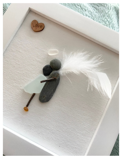 Sea Glass Memorial Framed Art Angel made with pebble embracing a human body with sea glass. Angel has a feather wing, pebble body and halo with a wooden love heart wall art or Desk Top Decor