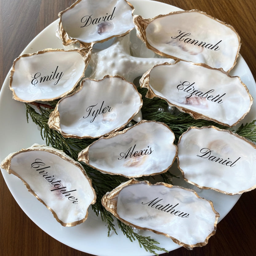 Oyster shells with names engraved on them, arranged on a white plate with greenery.