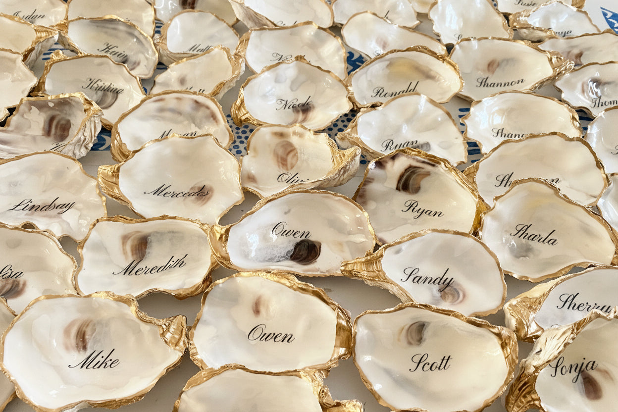 Oyster shells place cards and favors with names engraved on them arranged in a pattern.