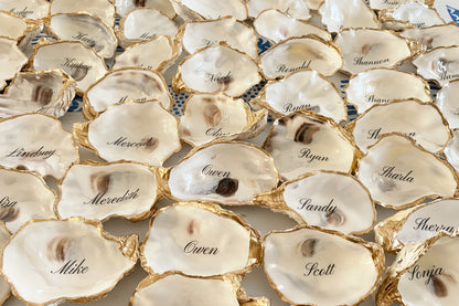 Oyster shells place cards and favors with names engraved on them arranged in a pattern.