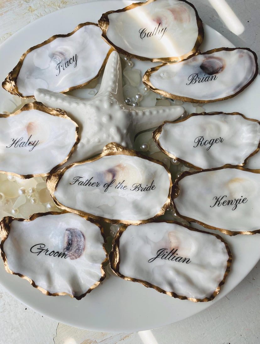 Oyster shells with names inscribed on them arranged on a white plate.