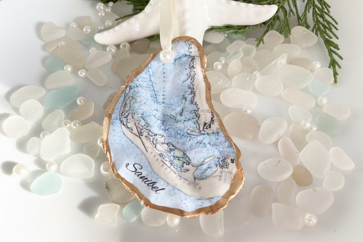 A personalized Sanibel Island oyster shell Christmas ornament with a map design, featuring a white and blue color scheme and the name 'SANIBEL' on the map.
