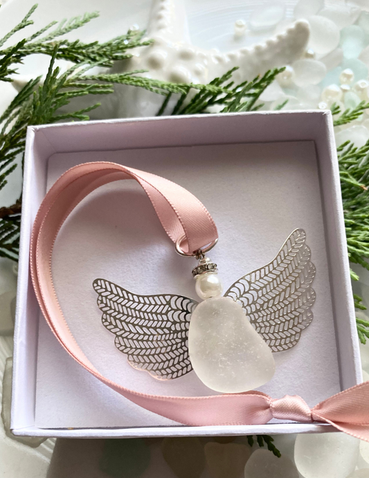 Sea glass angel ornament with a whitish sea glass body, silver metal wings, a rose gold satin ribbon hanger, and a cream pearl-like head inside of a white gift box