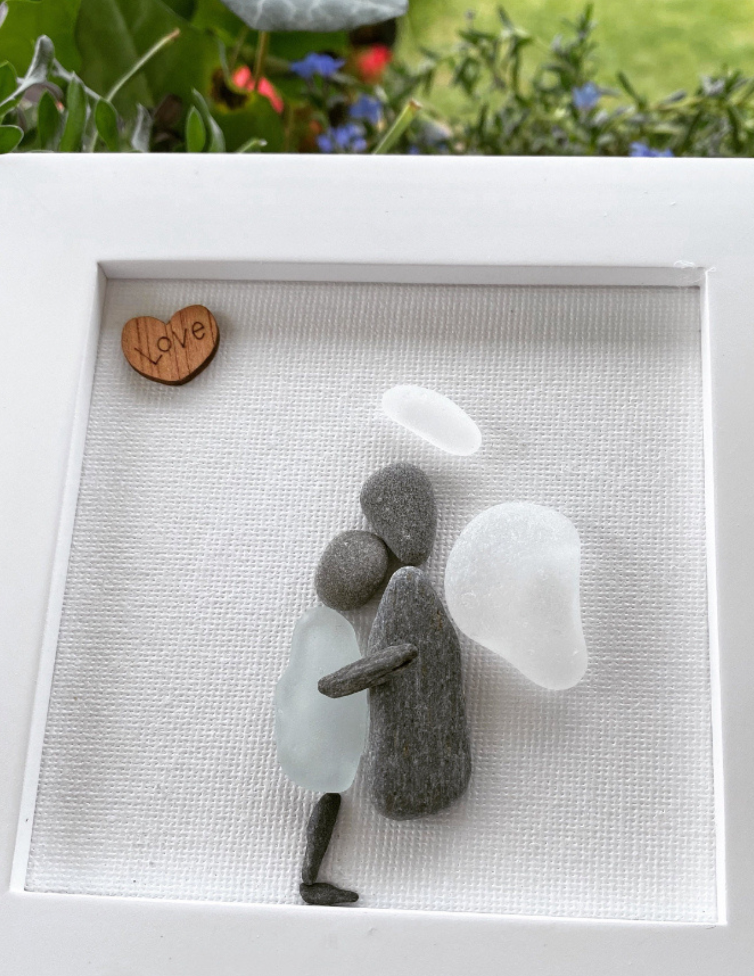 Sea Glass Memorial Framed Art Angel made with pebble embracing a human body with sea glass. Angel has a feather wing, pebble body and halo with a wooden love heart wall art or Desk Top Decor