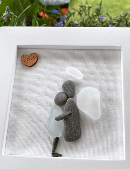 Sea Glass Memorial Framed Art Angel made with pebble embracing a human body with sea glass. Angel has a feather wing, pebble body and halo with a wooden love heart wall art or Desk Top Decor