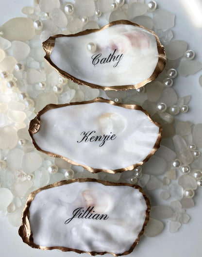 Three oyster shells with gold rims and names engraved on a pearl-studded background