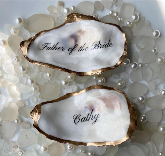 Two oyster shells with 'Father of the Bride' and 'Cathy' engraved on a pearl background