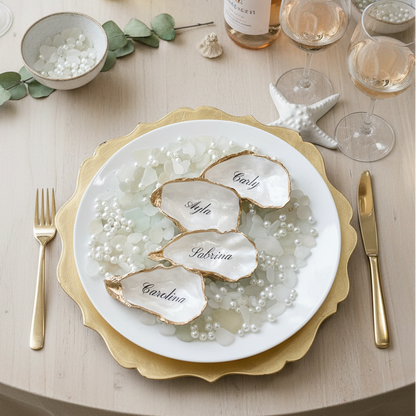Decorative table setting with oyster name cards on a white plate, gold rim, and pearl embellishments.