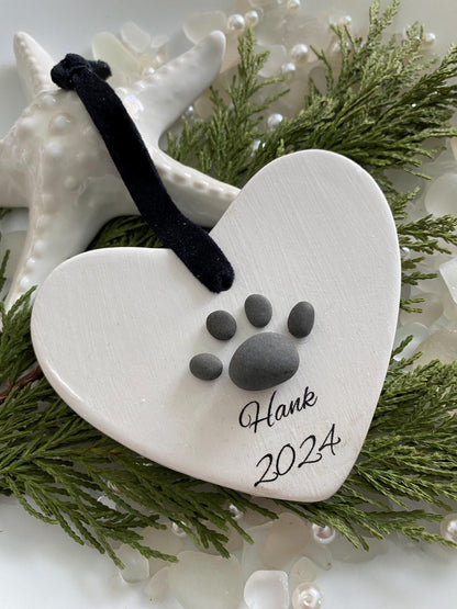 A ceramic heart-shaped ornament with a dog paw print design, personalized with a black ribbon 
