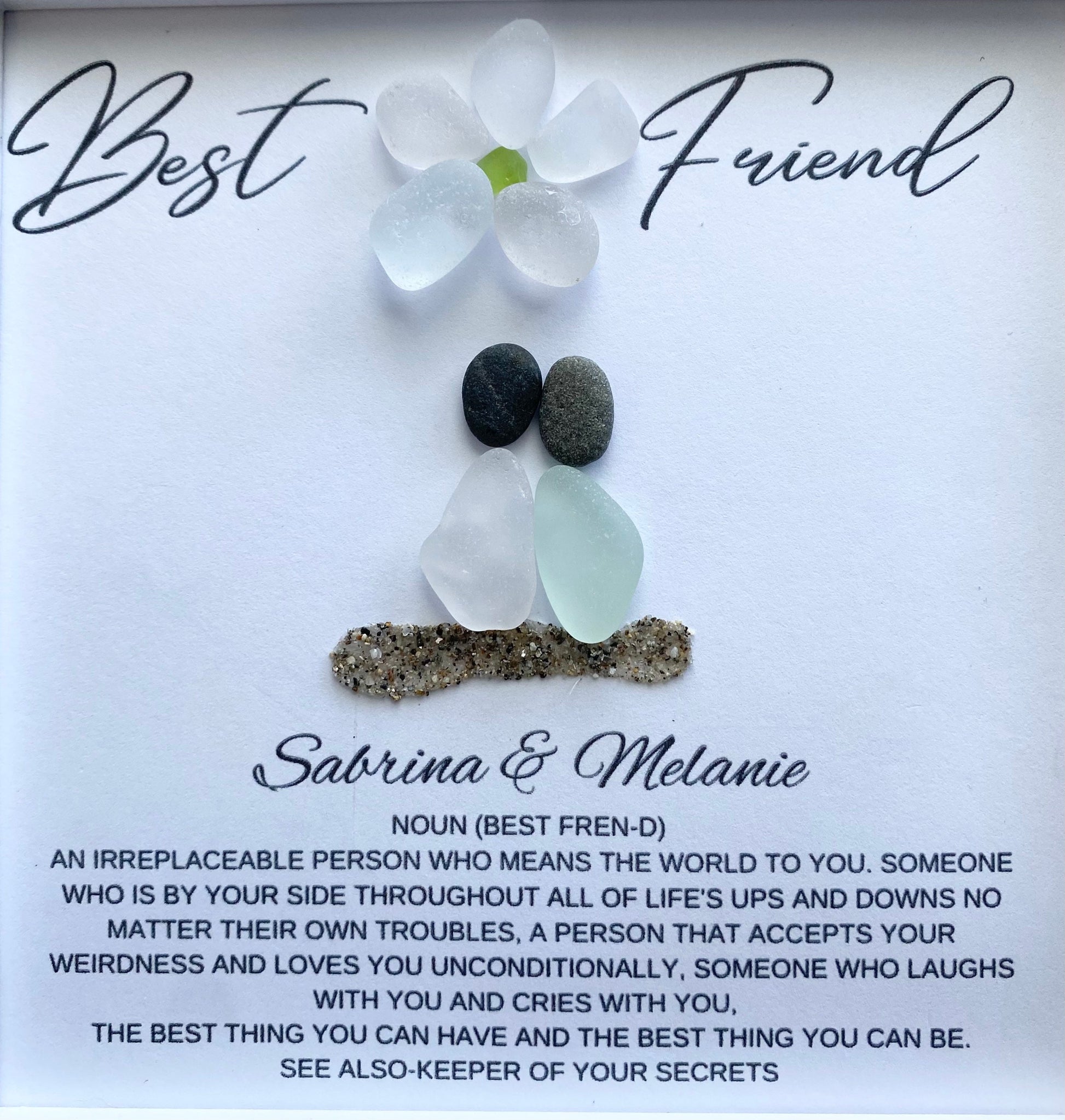 two sea glass friends with pebble heads sitting together on sand with their names and a quote below 