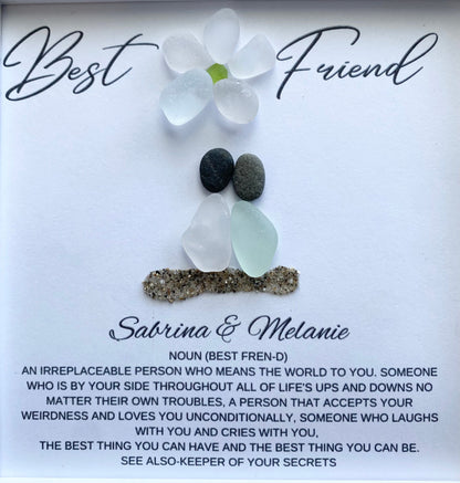 two sea glass friends with pebble heads sitting together on sand with their names and a quote below 