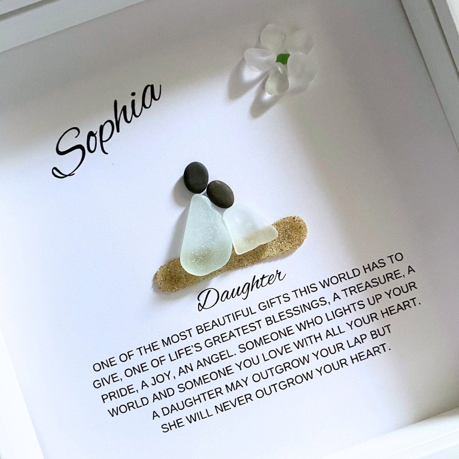 A framed pebble art piece with sea glass and stones, personalized with the name 'Sophia' and a message from a mother to her daughter.