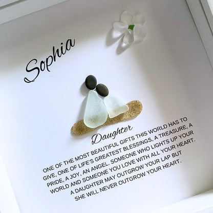 A framed pebble art piece with sea glass and stones, personalized with the name 'Sophia' and a message from a mother to her daughter.