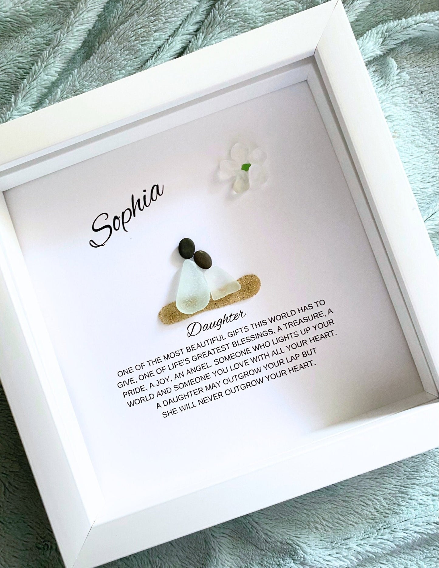 A framed pebble art piece with sea glass and stones, personalized with the name 'Sophia' and a message from a mother to her daughter.