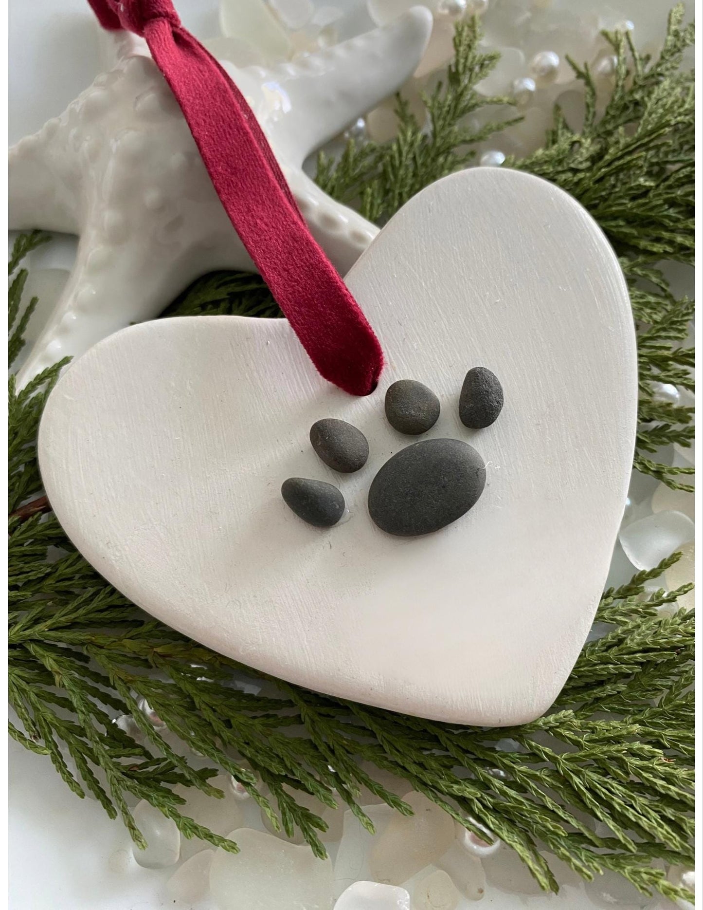 A ceramic heart-shaped ornament with a dog paw print design, personalized with a red ribbon 