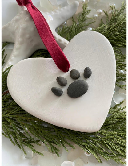 A ceramic heart-shaped ornament with a dog paw print design, personalized with a red ribbon 