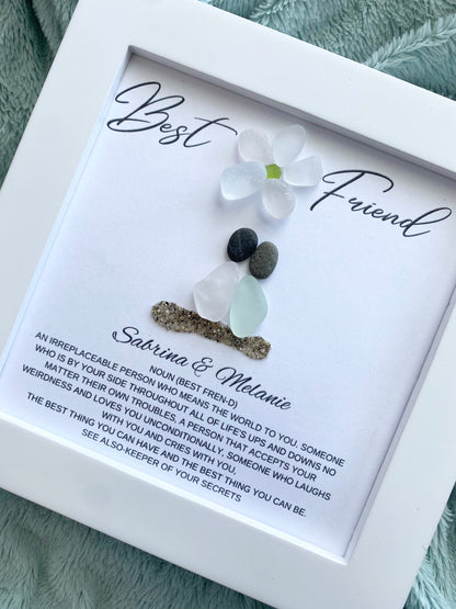 two sea glass friends with pebble heads sitting together on sand with their names and a quote below in a white frame