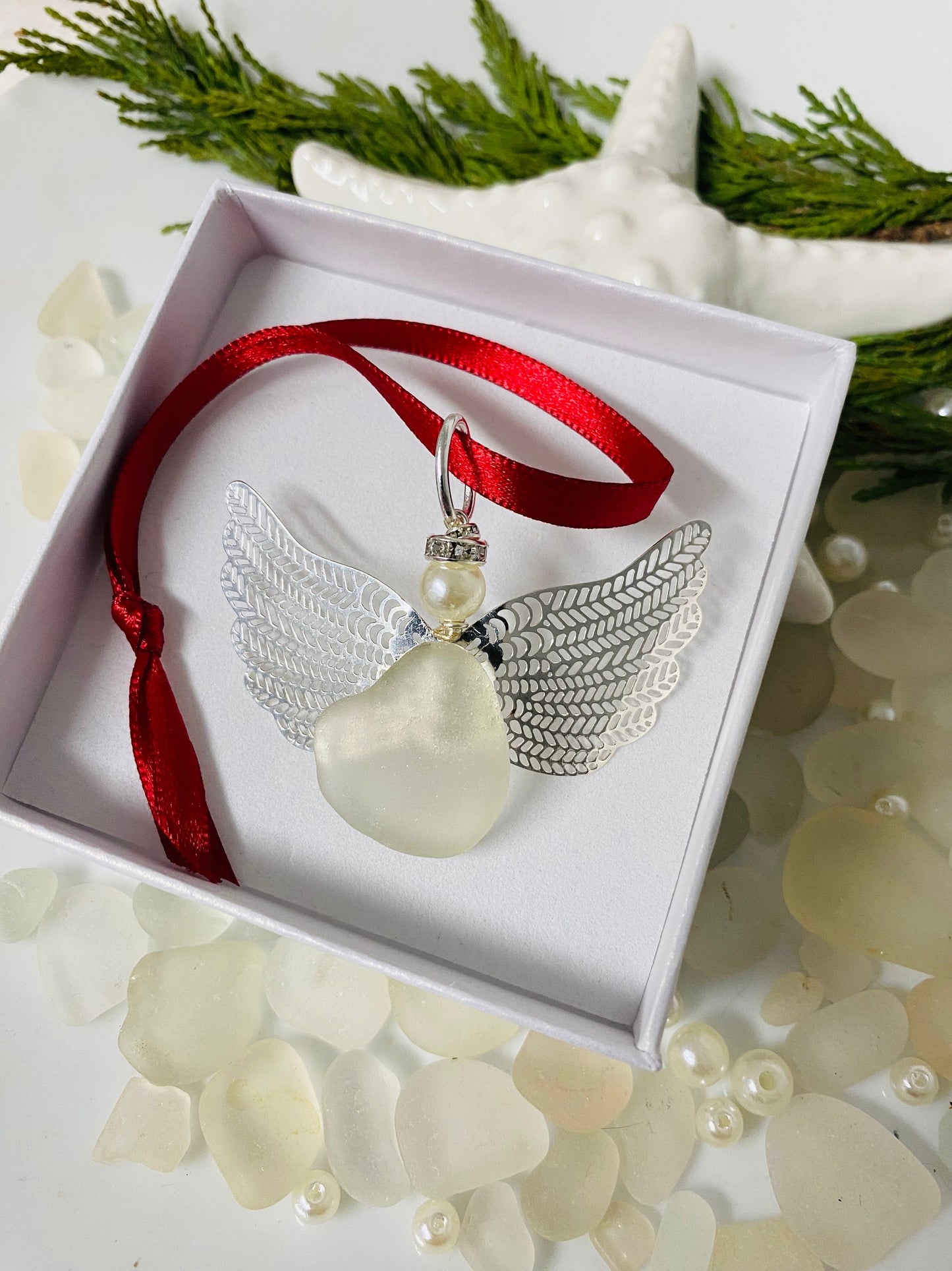 A handcrafted sea glass angel Christmas ornament with a red ribbon, displayed in a white jewelry box