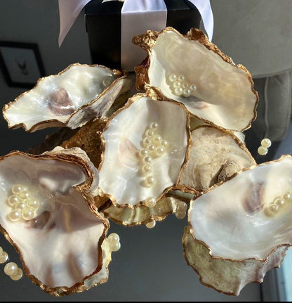 A decorative oyster shell ring dish with a glossy finish and gold leaf trim, displayed as a bridal party gift with pearl accents.