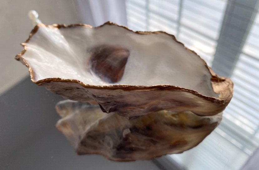 A decorative oyster shell ring dish with a glossy finish and gold leaf trim, displayed as a bridal party gift with pearl accents.
