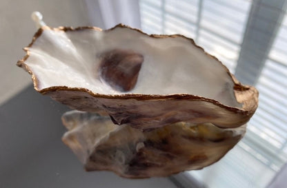 A decorative oyster shell ring dish with a glossy finish and gold leaf trim, displayed as a bridal party gift with pearl accents.