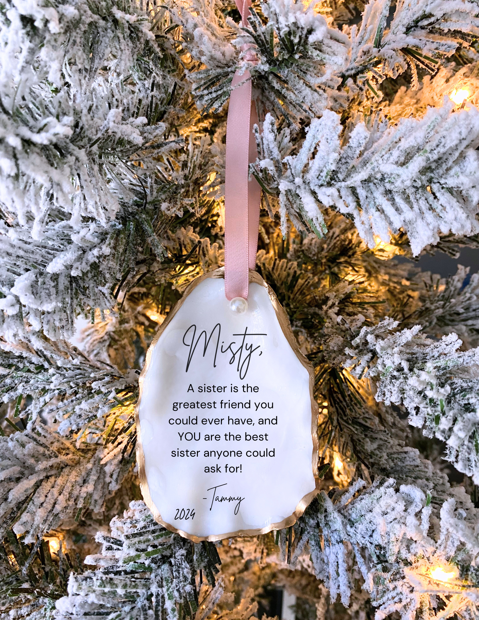 A personalized Christmas ornament oyster shell design, featuring a quote about being a sister, hanging on a christmas tree