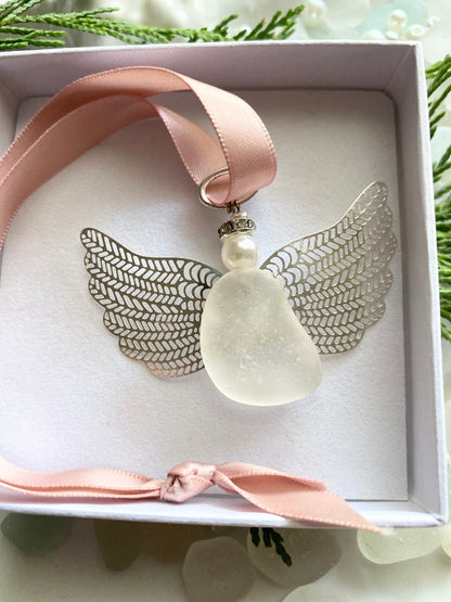 Sea glass angel ornament with a whitish sea glass body, silver metal wings, a rose gold satin ribbon hanger, and a cream pearl-like head inside of a white gift box