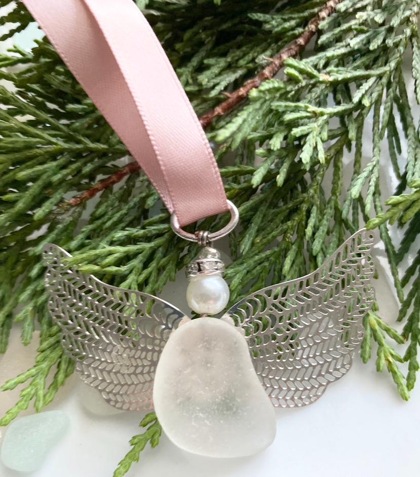 Sea glass angel ornament with a whitish sea glass body, silver metal wings, a rose gold satin ribbon hanger, and a cream pearl-like head 