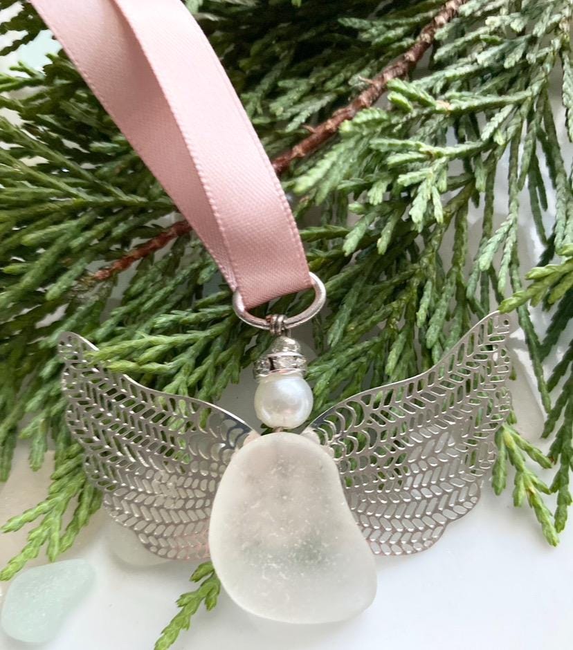 Sea glass angel ornament with a whitish sea glass body, silver metal wings, a rose gold satin ribbon hanger, and a cream pearl-like head