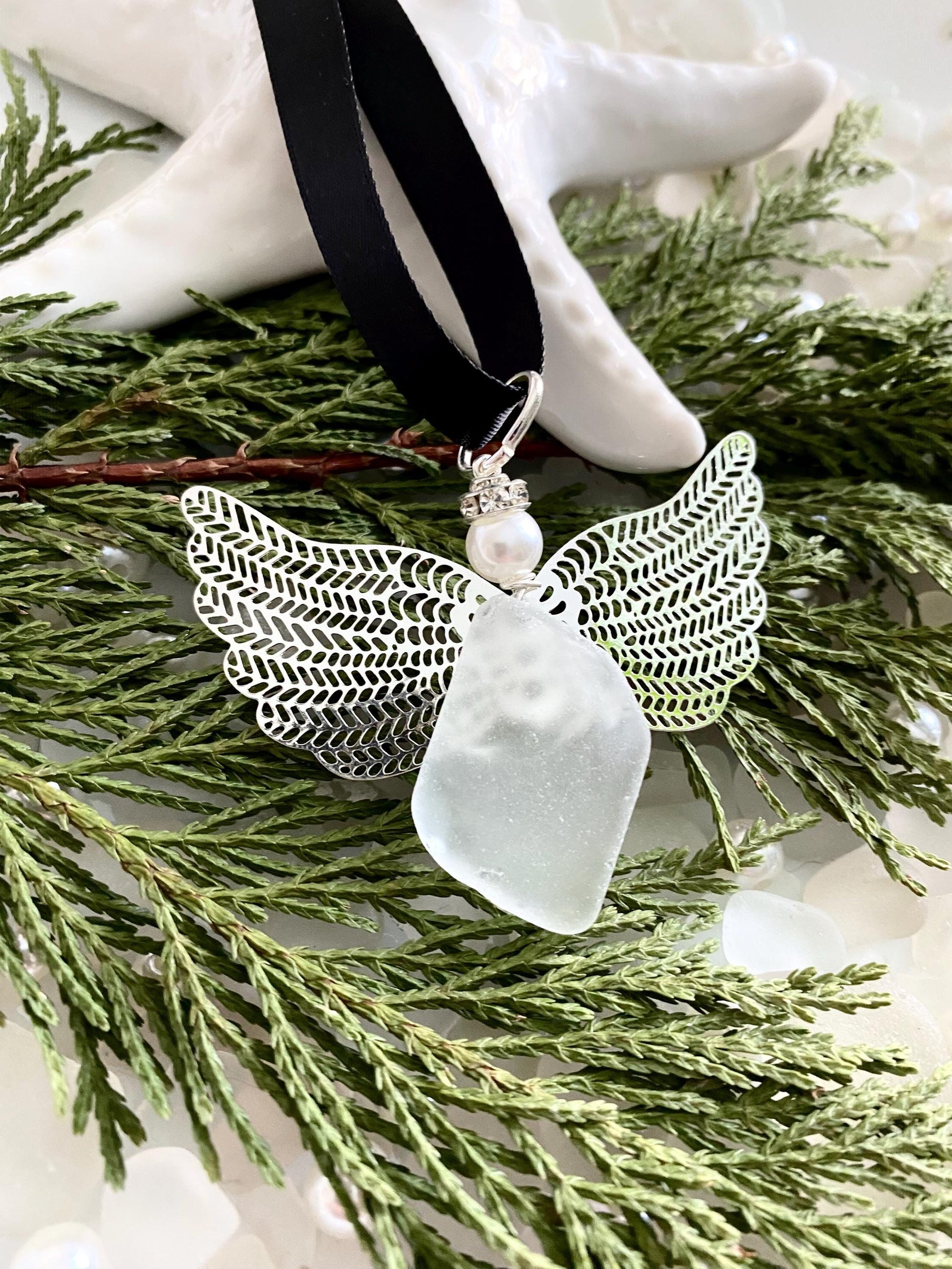 Sea glass angel ornament with a whitish sea glass body, silver metal wings, a black satin ribbon hanger, and a cream pearl-like head