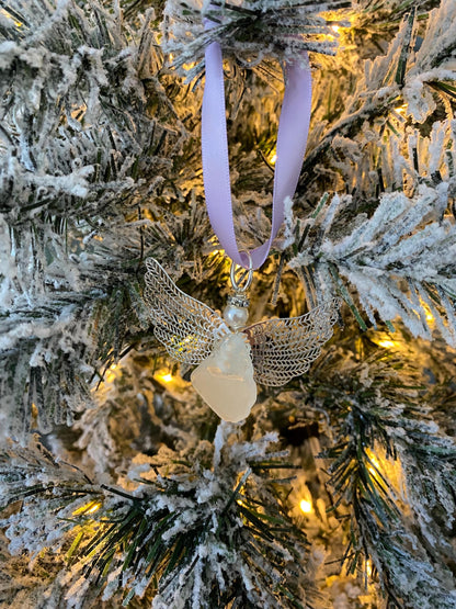 Sea glass angel ornament with a whitish sea glass body, silver metal wings, a lavender satin ribbon hanger, and a cream pearl-like head hanging on a Christmas tree