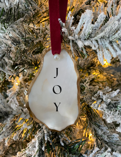 joy oyster shell ornament with pearl and red ribbon hanging from a Christmas tree