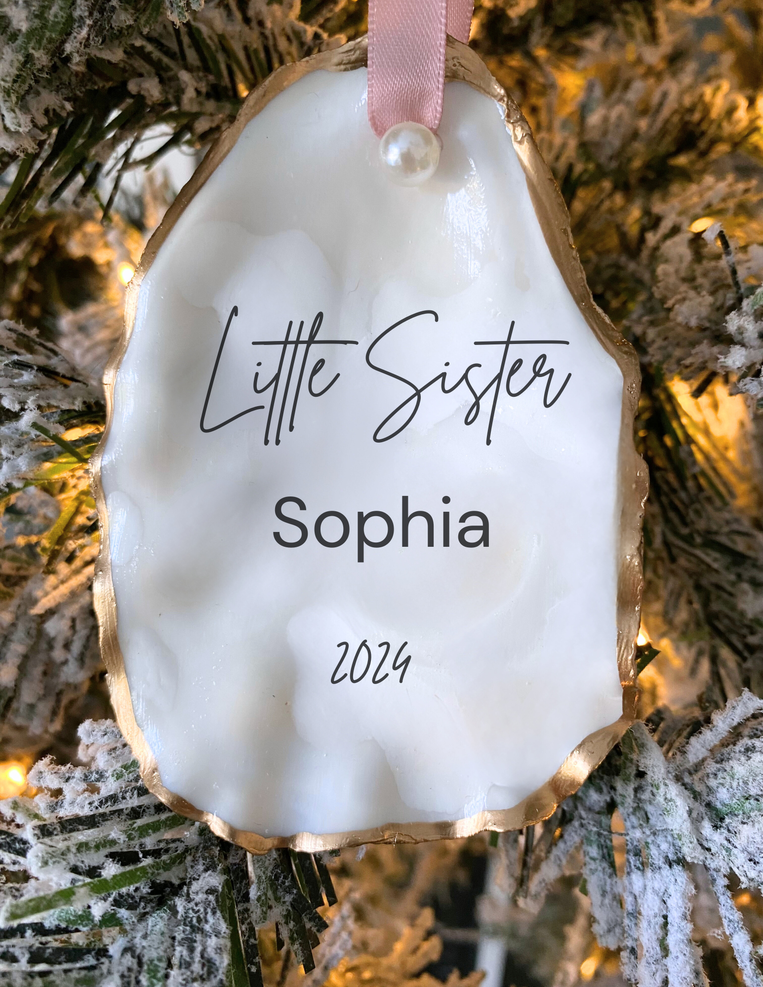 Personalized little sister oyster shell ornament with Sophia in script, pearl finish, gold trim, and pink ribbon displayed in a white gift box