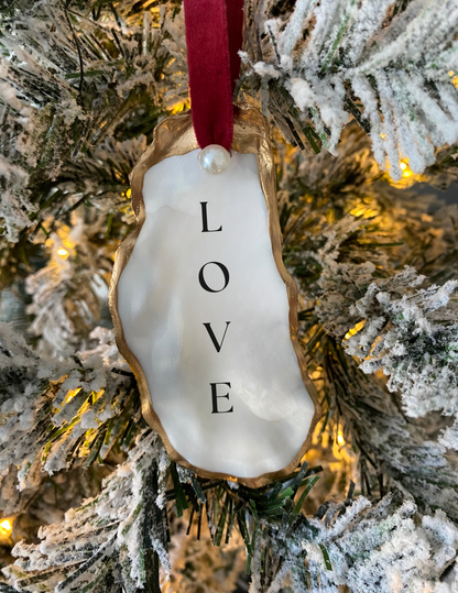 love oyster shell ornament with pearl and red ribbon hanging from a Christmas tree
