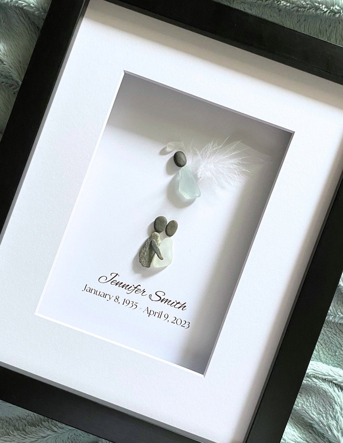 Framed artwork with pebble art and feather, personalized with names and dates.