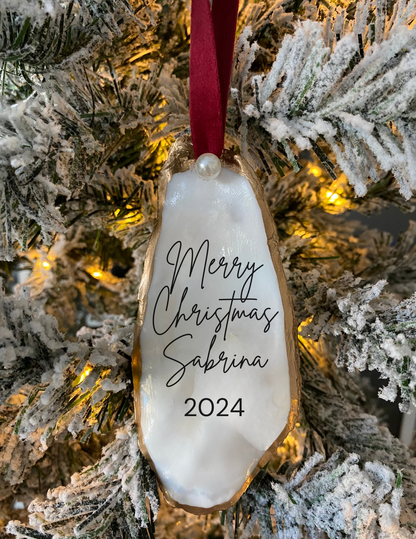 Oyster shell ornament with Merry Christmas wording, personalized date, gold trim, and red ribbon displayed as a holiday keepsake gift