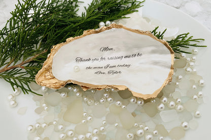 Oyster shell with engraved message surrounded by greenery and pearls