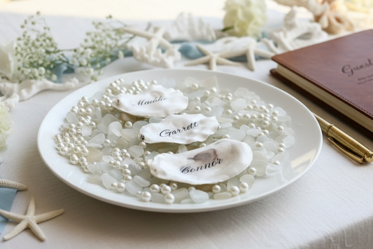 Decorative plate with engraved names on oyster shell place cards surrounded by pearls and starfish.