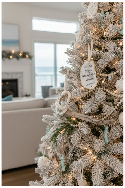 A personalized oyster shell Christmas ornament with the text 'Mr & Mrs' and a date '10/1/2022' on it, hanging from a branch with pearl-like beads and greenery in the background.