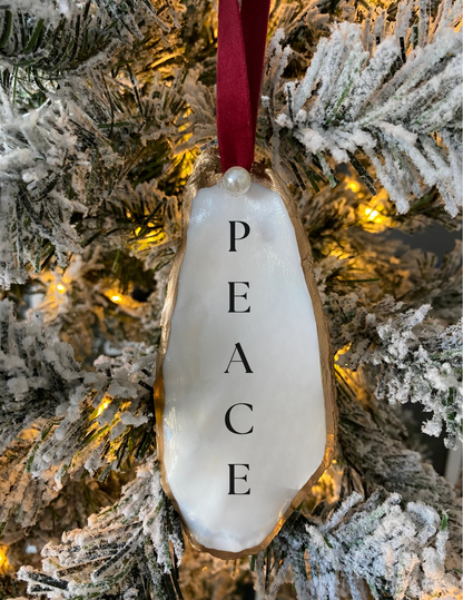 peace oyster shell ornament with pearl and red ribbon hanging from a Christmas tree