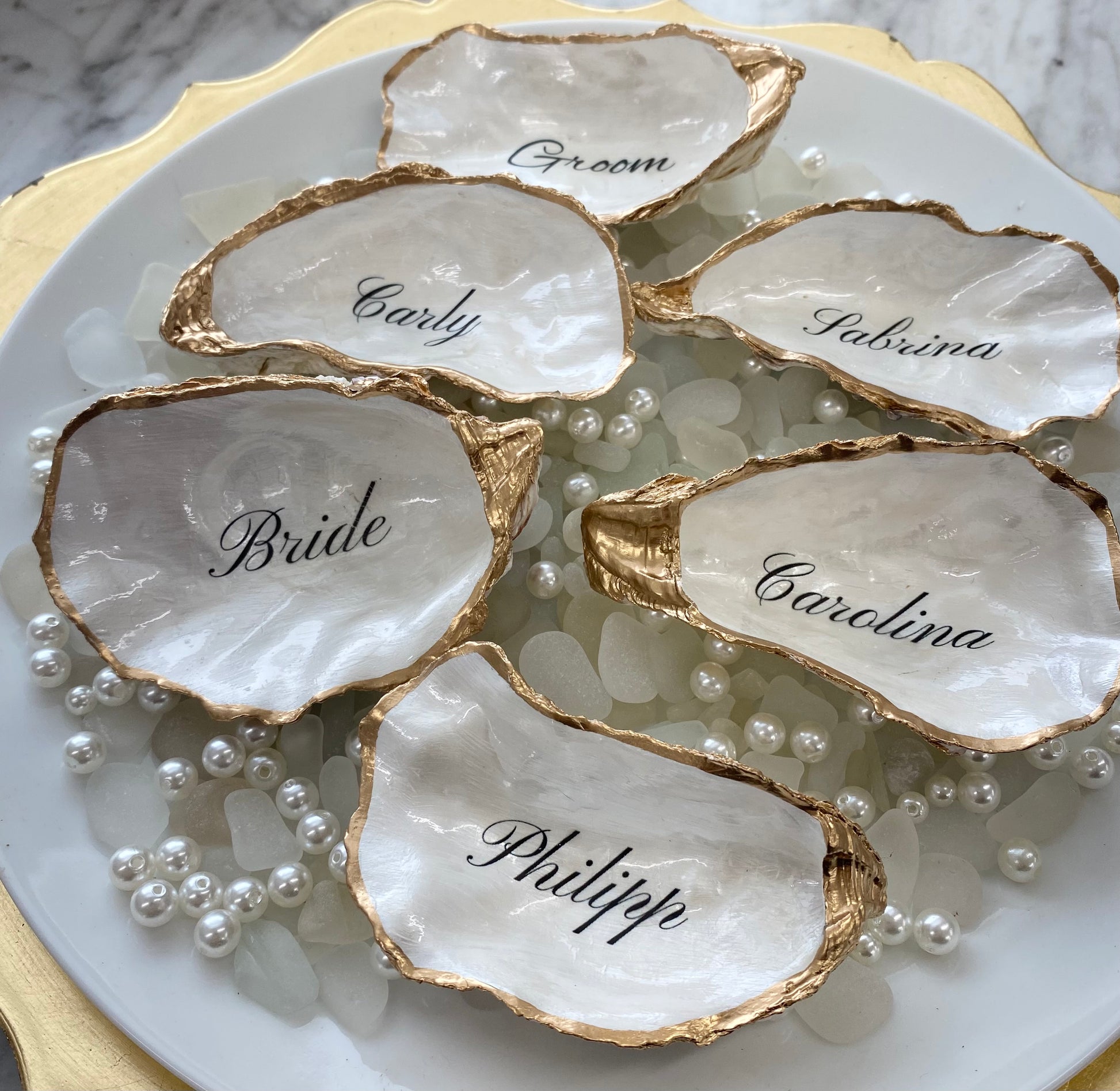 Oyster shell place cards with names engraved on them, placed on a marble surface with pearls.