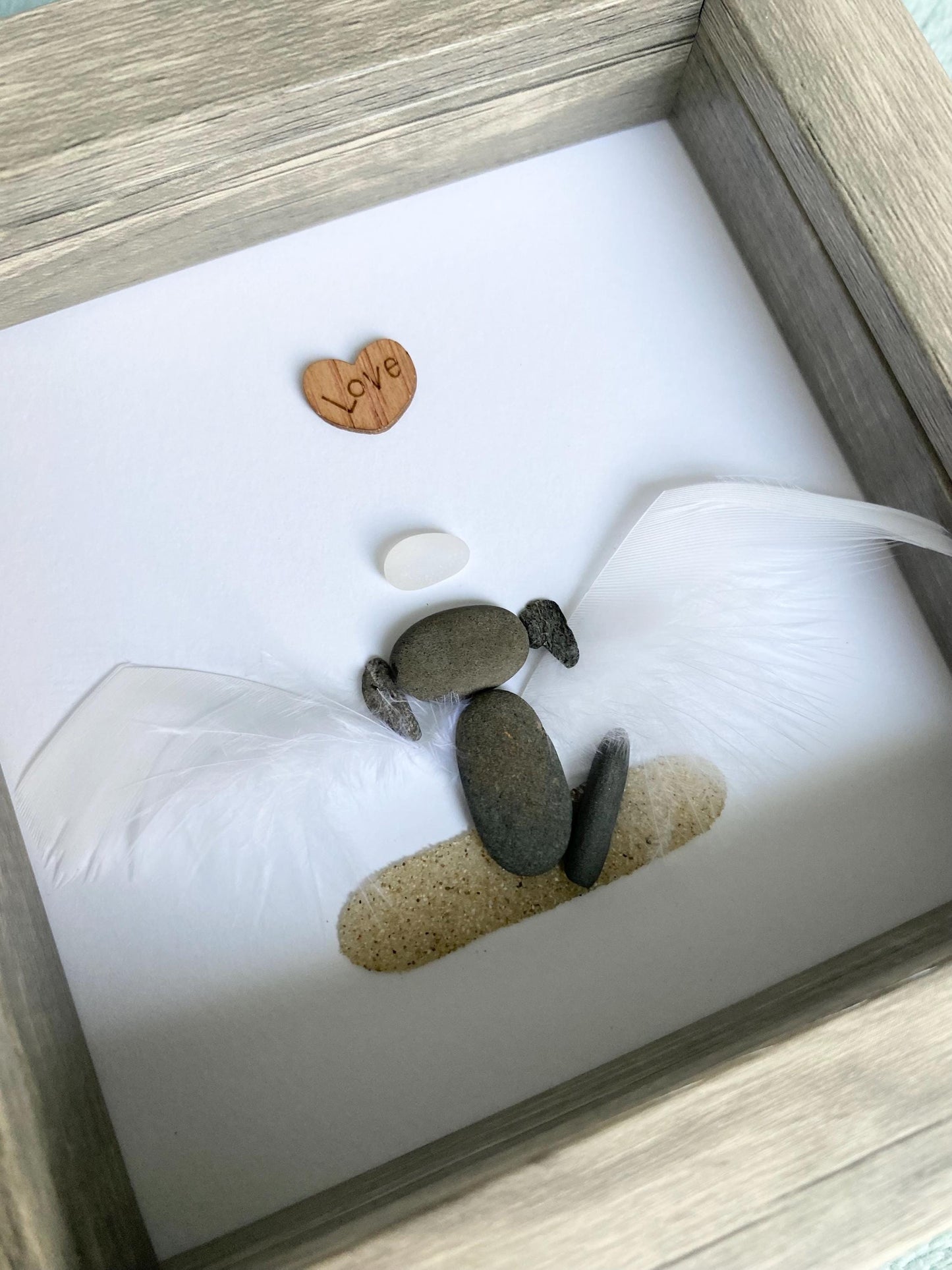 A personalized dog memorial gift featuring a white sea glass and pebble art piece with a shadowbox frame.