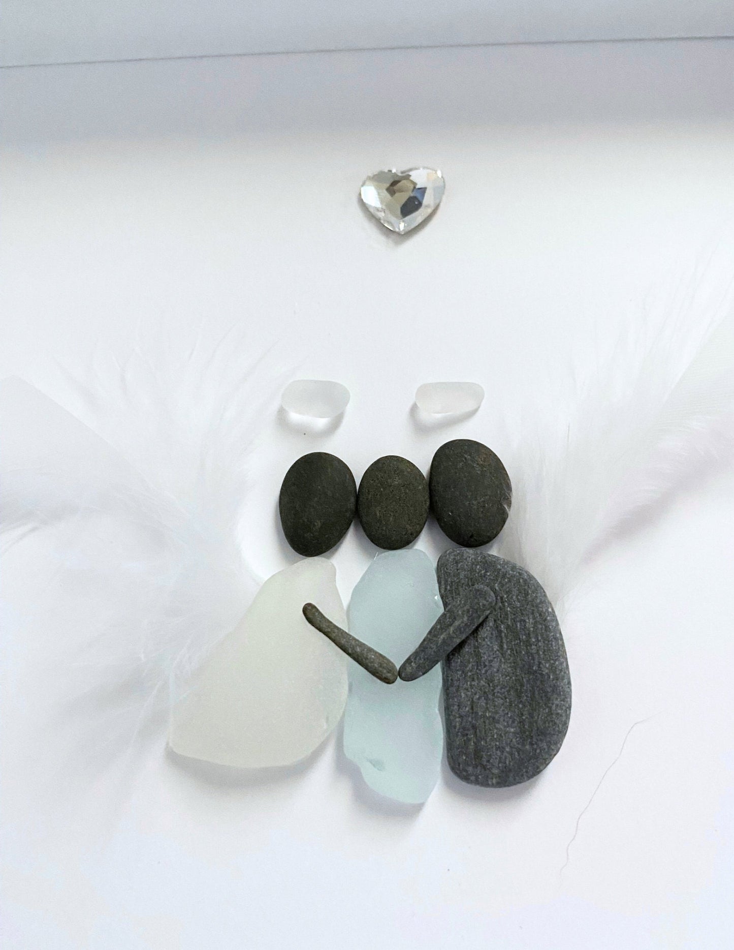 A memorial gift featuring a sea glass art piece with a feather wings hugging a sea glass human, displayed on a white surface.