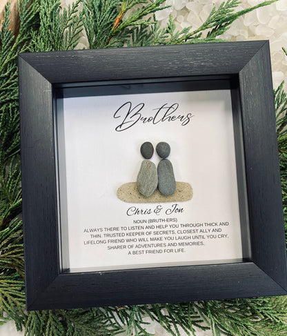 Two pebble brothers sitting next to each other with their names under and a short quote. Featured in a black frame.