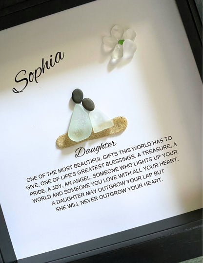 A framed pebble art piece with sea glass and stones, personalized with the name 'Sophia' and a message from a mother to her daughter.