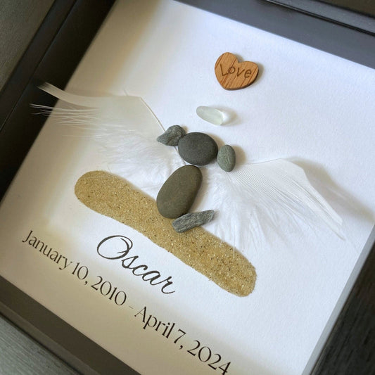 A personalized dog memorial gift featuring a white sea glass and pebble design with the name 'Oscar' and birth and death dates on a shadowbox frame.