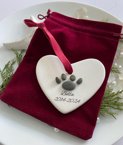 A ceramic heart-shaped ornament with a dog paw print design, personalized with a red ribbon 