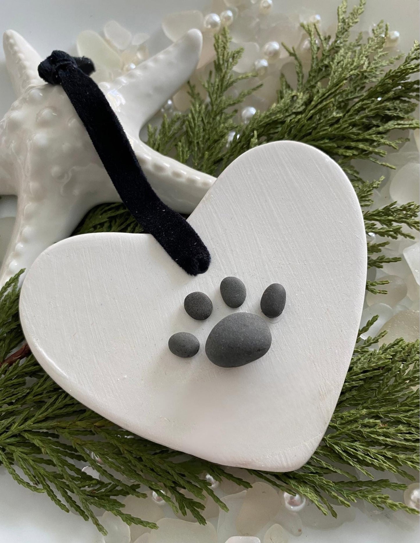 A ceramic heart-shaped ornament with a dog paw print design, personalized with a black ribbon 